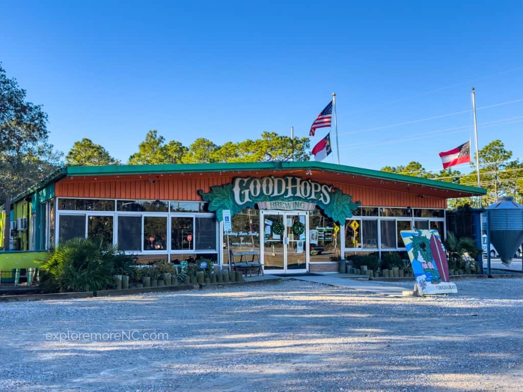 The front of Good Hops Brewing, a local brewery in Carolina Beach, featuring a green and orange façade with flags flying, inviting visitors to enjoy craft beers.
