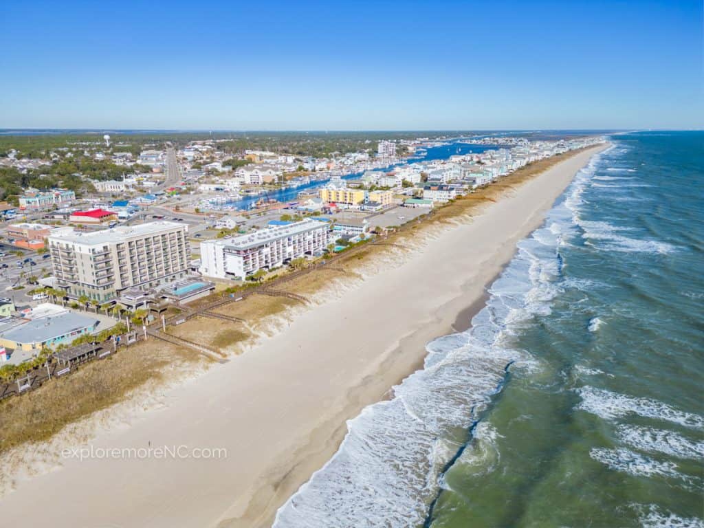 A sweeping aerial view of Carolina Beach, with the beach on one side and the town on the other, highlighting the density of buildings and the long, narrow strip of the beach.