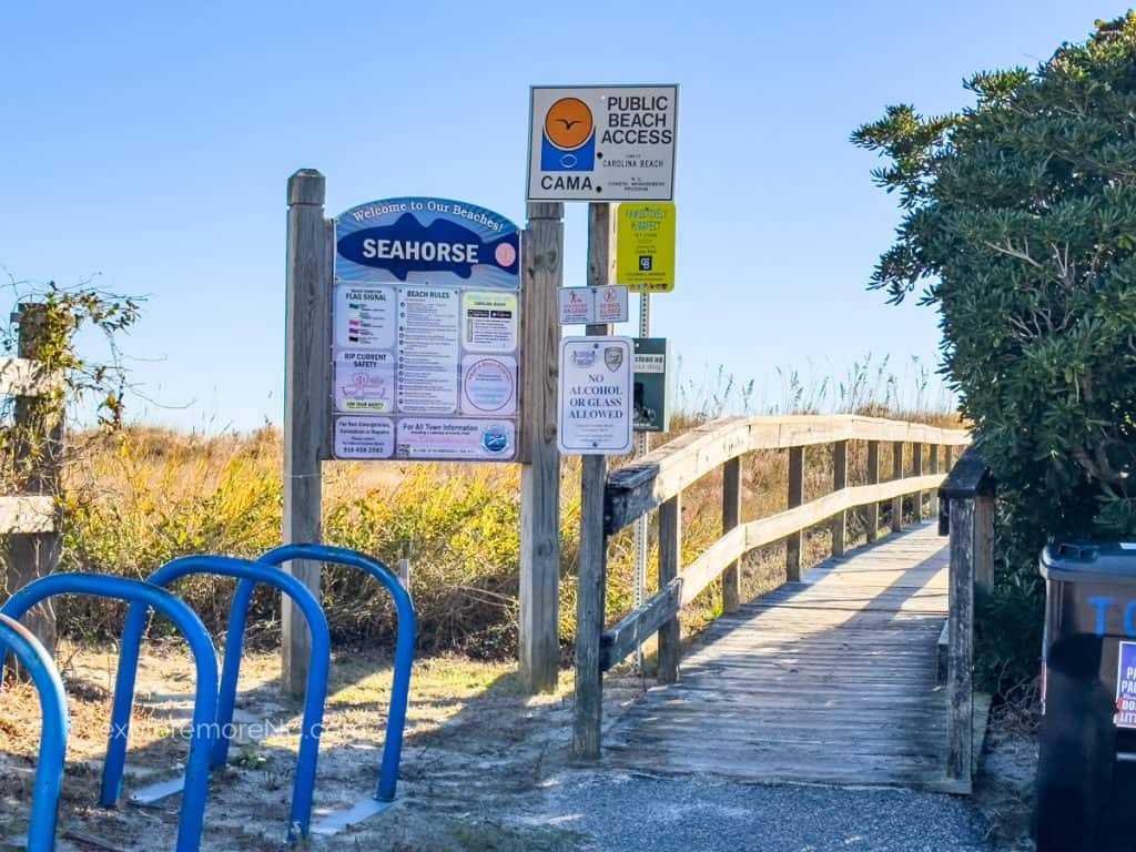 The entrance to "Seahorse" beach access, featuring a wooden boardwalk that leads to the beach. Informational signs provide safety and regulation details, with clear skies above.